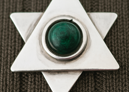 Sterling silver Star of David pendant with a polished green malachite stone at its center, shown in close-up against a textured dark fabric background.